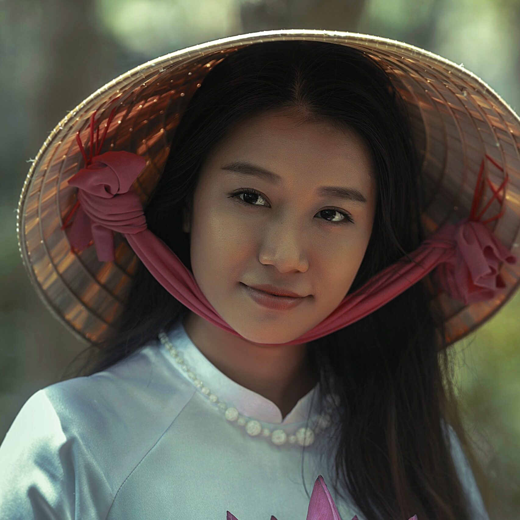 woman wearing white long-sleeved dress and brown sungat holding pink petaled flower